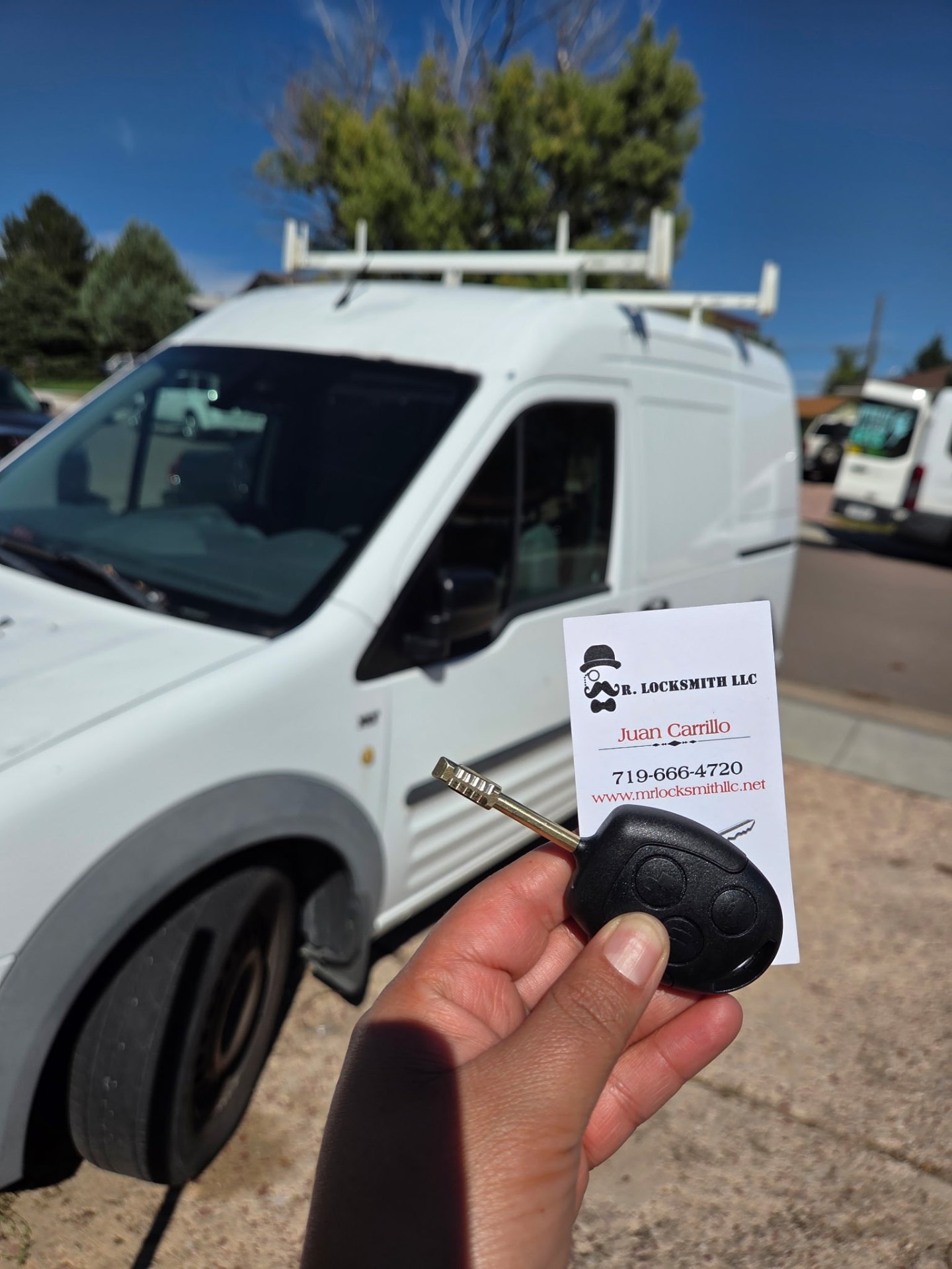 New Ford Tibbe remote key held with Mr. Locksmith business card in front of the locksmith van